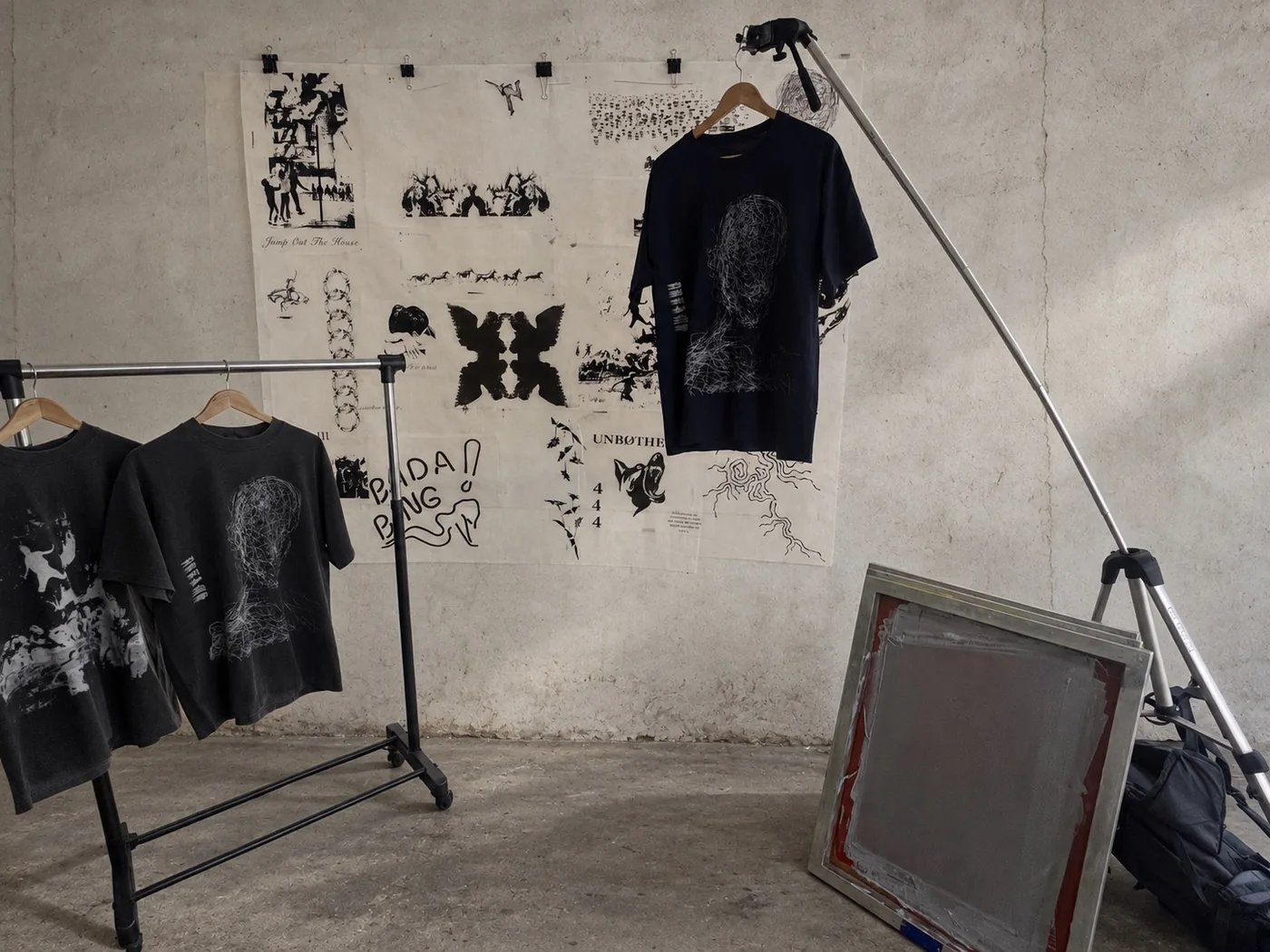 Dreams tees, clothing racks and print screens with transparencies against an edited warehouse concrete wall